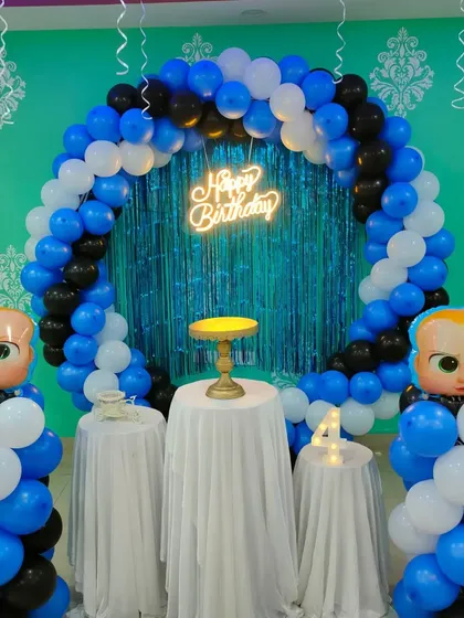 A Boss Baby theme featuring a blue and black balloon ring with a shiny tinsel backdrop. Large foil Boss Baby heads are placed on balloon pillars.