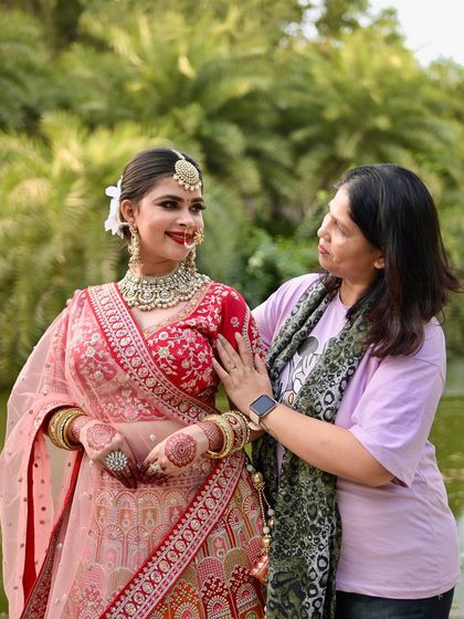 A heartwarming behind-the-scenes moment between the makeup artist and the model, wearing our red and pink lehenga.