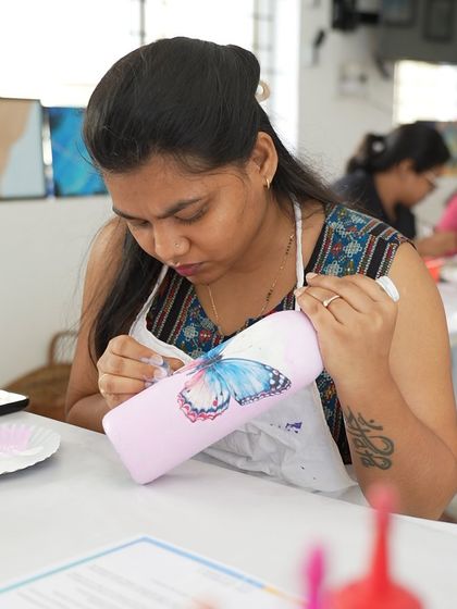 A participant paints a butterfly design on her decoupage bottle. The workshop allows you to combine painting with the decoupage technique.