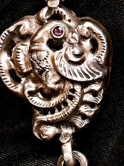A detailed look at a handcrafted silver peacock pendant from a tribal-patterned necklace. The intricate carving and single red stone eye highlight the folk artistry of rural Rajasthan.