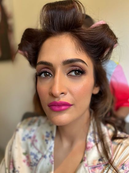 A pre-styling shot showing the bold fuchsia lip color for Deepali's Haldi. Even with her hair in rollers, the makeup already makes a powerful and beautiful statement.