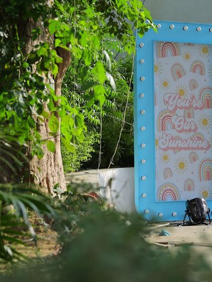 A blue marquee sign with a "You Are Our Sunshine" graphic, partially hidden by foliage. This shows how I integrate decor elements into the natural landscape of an outdoor venue.