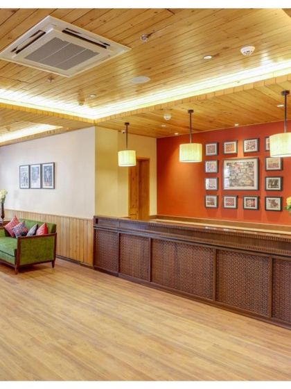 A wider view of the reception and lobby area, showcasing the extensive use of local pine wood and a color palette inspired by the Himachali landscape.