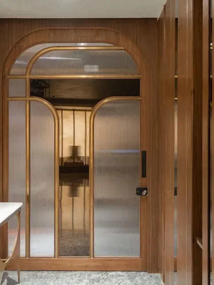 Here, the main door with its arched, fluted glass panels is designed to recede into a pocket, allowing the custom foyer console and vertical wood slat wall to take center stage. This creates a layered and welcoming entrance that feels both grand and intimate.