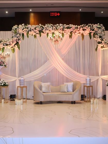 This elegant reception stage features soft, flowing white drapes and a beautiful arch of white and pink florals. The design is minimalist yet romantic, perfect for a sophisticated and modern couple.