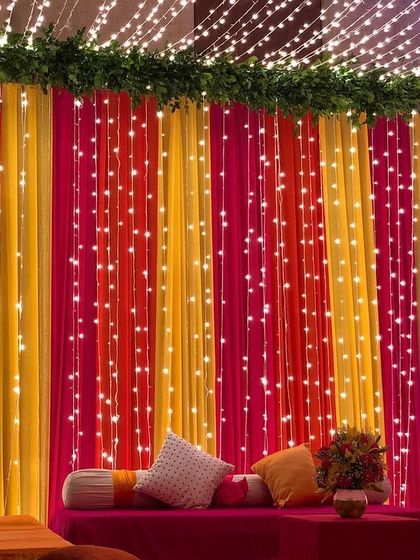 An elegant Mehendi seating area with vibrant drapes and a canopy of fairy lights, creating a magical and festive atmosphere.