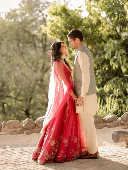 A sweet moment between the couple during their coastal Sangeet. Her bright Ridhi Mehra lehenga pops against the lush green background, and his subtle vest adds a touch of coordinated color.
