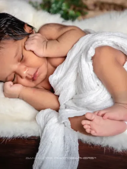 A peaceful slumber. The simple white wrap and fluffy pillow create a cloud-like bed for this sleeping angel.
