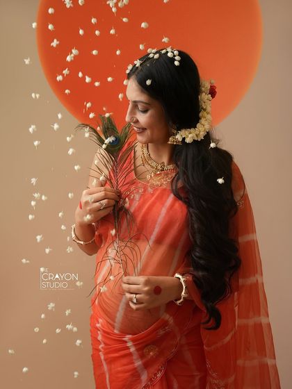 A close up portrait highlighting the traditional details, from the flowers in her hair to the peacock feather she holds. Her gentle smile reflects her inner joy.