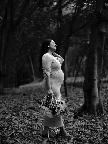 A dramatic black and white portrait of the mom-to-be in a forest, holding a basket of flowers. The contrast and composition are striking and artistic.