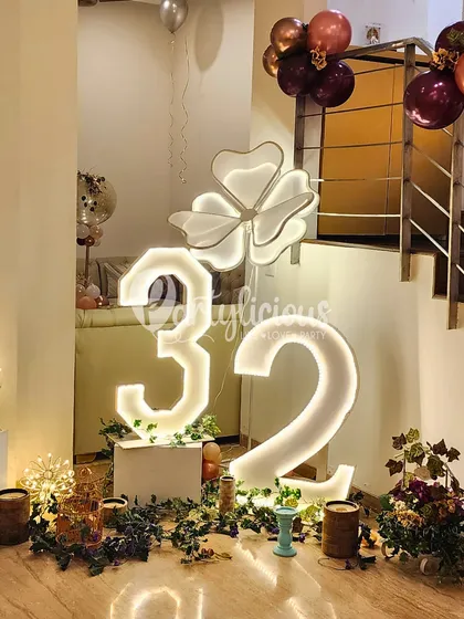 Light up the night with these large, illuminated marquee numbers for a 32nd birthday, surrounded by lush greenery and floral-shaped lights.