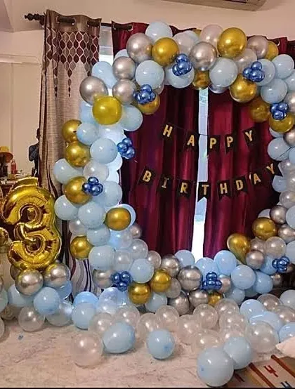 A blue, silver, and gold circular balloon arch set up for a home birthday party.
