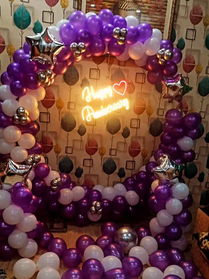 An anniversary decoration with a purple and white theme. This full balloon ring with a "Happy Anniversary" neon sign creates a beautiful and vibrant photo booth area.