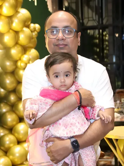 A father holds his baby girl in front of a golden balloon backdrop. The warm lighting creates a beautiful portrait.