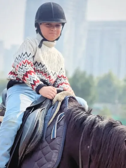 A focused young rider in a cozy sweater, ready for his session in the arena. We provide a safe environment for kids to build their confidence with horses.