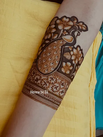 A close-up of an armband featuring a beautiful peacock surrounded by flowers. This shows how the design continues elegantly up the arm.