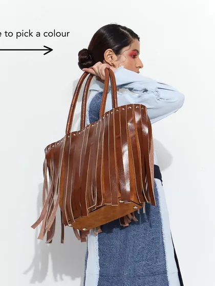 A model carrying the Tassel Tango Tote, showcasing its size and how it hangs. Swipe to see it in different colors.