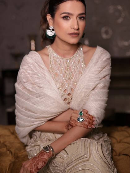 A client stuns in an ivory sharara set, a vision of elegance and grace with exquisite draped sleeves and rich embellishments.