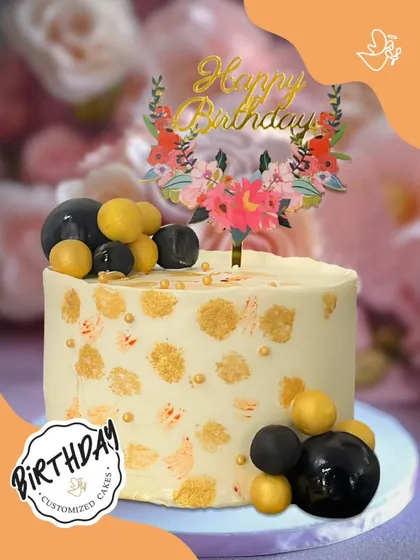 A chic and modern birthday cake with a gold-flecked design and a floral topper. The black and yellow spheres add a contemporary touch.