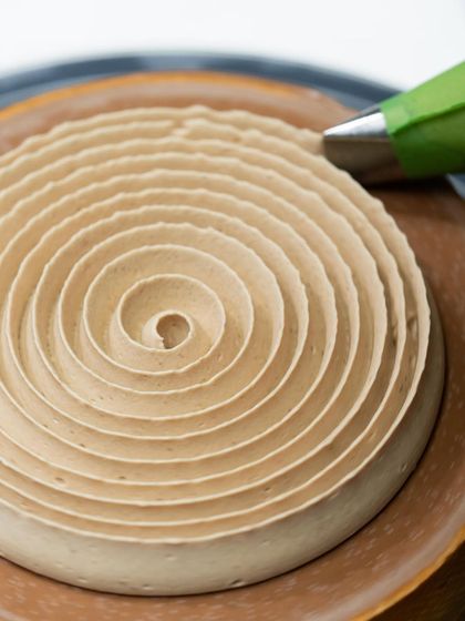 A mesmerizing spiral of cream being piped onto a tart.