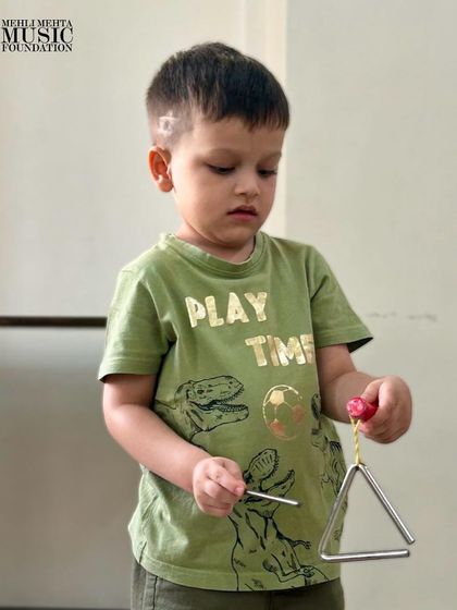 A young boy concentrates on playing the triangle. Learning to play even simple percussion instruments helps develop fine motor skills and a sense of rhythm.