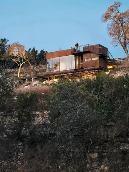 This is our vision for hillside living. A modular home built with a rustic, weathered steel exterior that blends into the rocky terrain, featuring a rooftop deck to take in the stunning views.