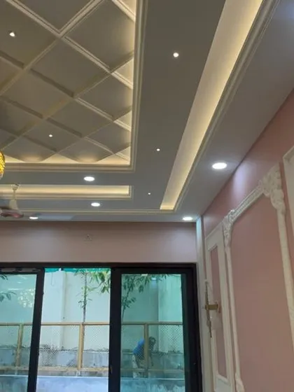 A coffered false ceiling with an elegant, modern chandelier. The combination of recessed lights and the statement fixture provides layered lighting for different moods and functions.