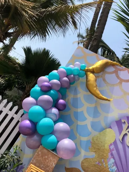 A glimpse of our magical mermaid-themed party decor. This outdoor setup includes a mermaid scale backdrop, a golden tail, and a balloon cascade in ocean-inspired shades of turquoise and purple.