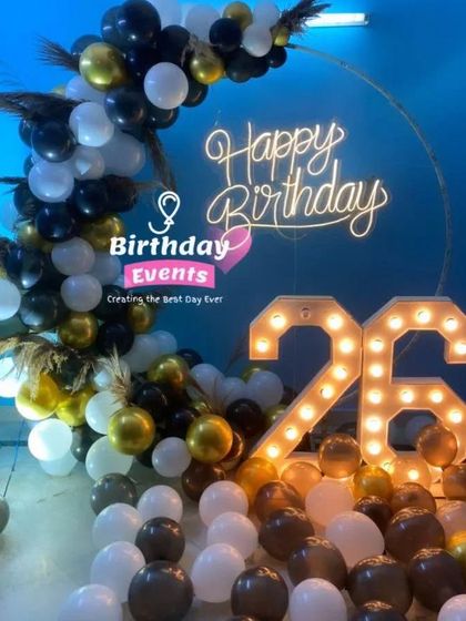 A chic setup for a 26th birthday, featuring black, white, and gold balloons, dried pampas grass accents, and large marquee numbers.