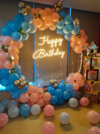 This fun balloon ring combines pastel pink, blue, and peach balloons with a 'Happy Birthday' neon sign. The scattered balloons at the base and the transparent letter boxes add a playful touch for a birthday celebration.
