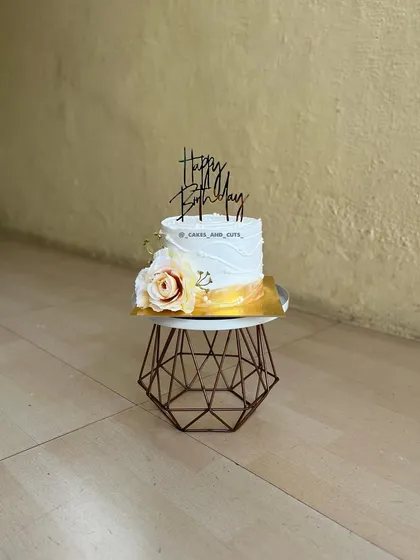 A simple and elegant birthday cake with a single yellow rose and a modern topper.