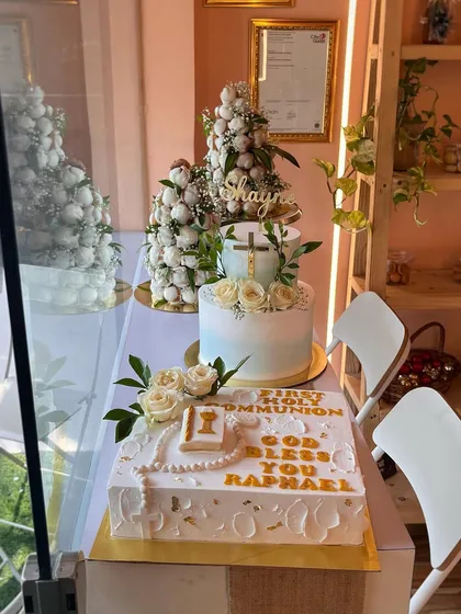 A glimpse of our Communion cake orders from a few Sundays back. This photo showcases a variety of designs, including a square cake with a rosary, a tiered cake with a cross, and croquembouche towers.