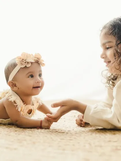 The beginning of a lifelong friendship. This sibling photoshoot captures a tender moment between a big sister and her new baby sister, highlighting the gentle connection in our natural, boho-inspired studio setting.