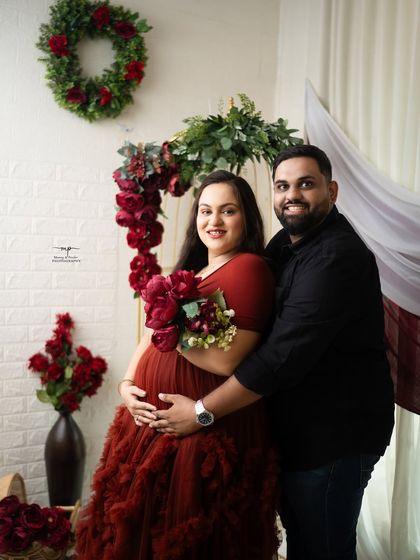 A beautiful portrait of the expecting couple. The mother-to-be holds a bouquet of red flowers, tying the whole elegant, color-coordinated theme together.