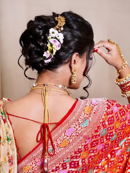 A detailed back view of a messy khopa. You can see the soft, interwoven sections of hair, adorned with a delicate spray of flowers and a golden accessory, creating a look that is both intricate and effortlessly beautiful.