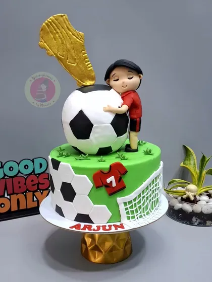 A cake for a young football lover, featuring a golden boot trophy, a large soccer ball, and a custom player figurine.