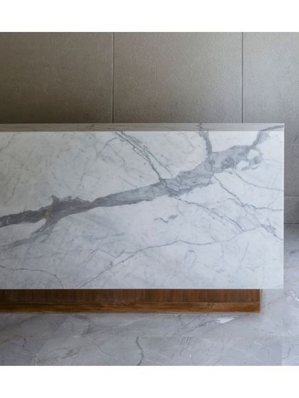A detail shot of the bold, veined marble used for a reception desk. The natural, art-like pattern of the stone becomes the primary design element, set against a simple wooden base and concrete floor.