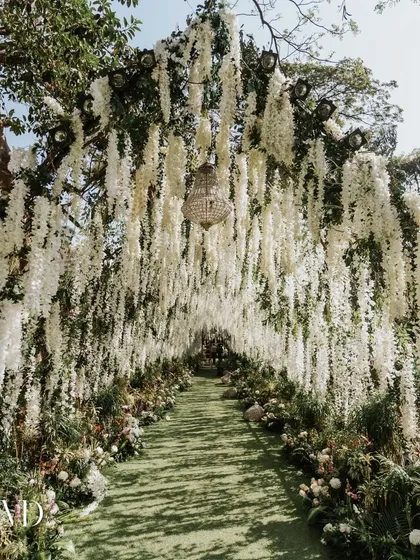 We designed this enchanting floral tunnel to create a magical entryway for a vintage-themed wedding. Guests walked through a path completely enveloped in hanging white wisteria and lush greenery.