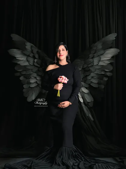 A different take on the black angel wings, this time with the mom-to-be holding a small bouquet, adding a touch of softness to the dramatic studio setup.