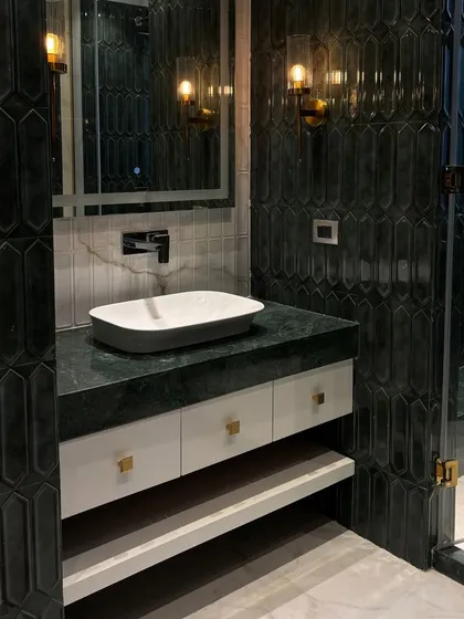 A close-up of a bathroom vanity with striking green hexagonal tiles, a modern vessel sink, and elegant wall sconces.