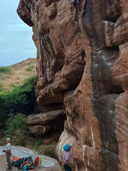 A wide view of the climbing area in Badami, showing the scale of the rock faces we explore. A climber and belayer prepare at the base of a route, ready for the ascent.