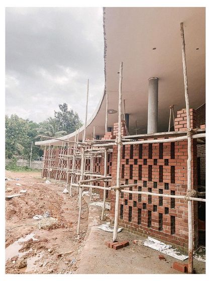 Construction progress on the auditorium's curved brick jali wall. This image shows the intricate pattern of the brickwork being laid, a traditional craft technique used to create a visually porous and ventilated facade.