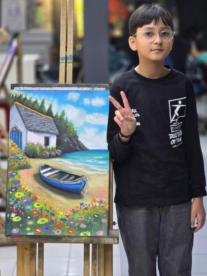 The young artist gives a peace sign as he stands next to his completed, colorful oil pastel landscape, proud of his beautiful creation.