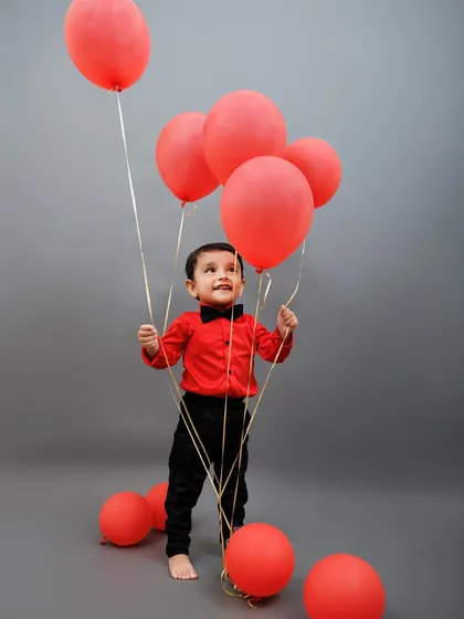 A toddler holds a bunch of red balloons, looking up with wonder during his second birthday session.
