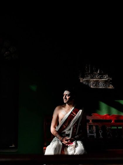 A groom sits in a quiet, contemplative moment, with dramatic lighting casting shadows across the room. A powerful and artistic portrait.