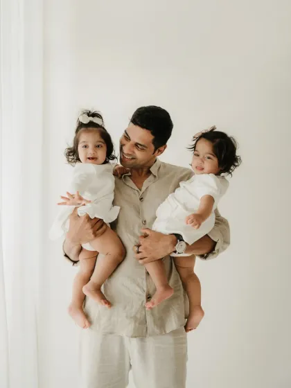 A proud father holds his twin daughters, one in each arm, with a huge smile. This is a wonderful portrait from a twin toddler session.