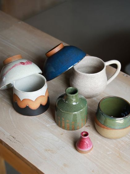 A colorful group of student creations, including lidded jars, mugs, and bowls with layered glazes and playful designs.