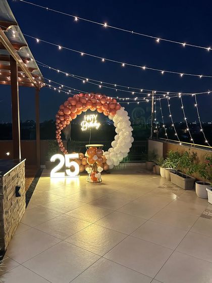 A stunning 25th birthday party on a rooftop terrace, with a rose gold and white balloon ring set against the evening sky.