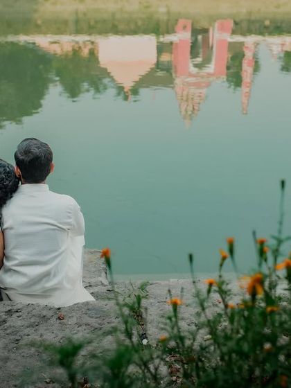 A reflective and romantic moment. The couple sits by a temple pond, their backs to the camera, looking at the reflection of the temple in the water.