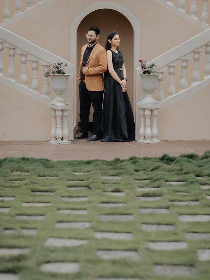 An elegant, full-length portrait at the base of a grand staircase, showcasing the couple's formal attire in a sophisticated setting.